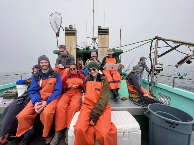 A group of people in orange waders gathered around on a boat