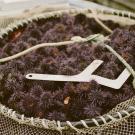 A woven basket full of small purple urchins with a metal measuring device on top of them